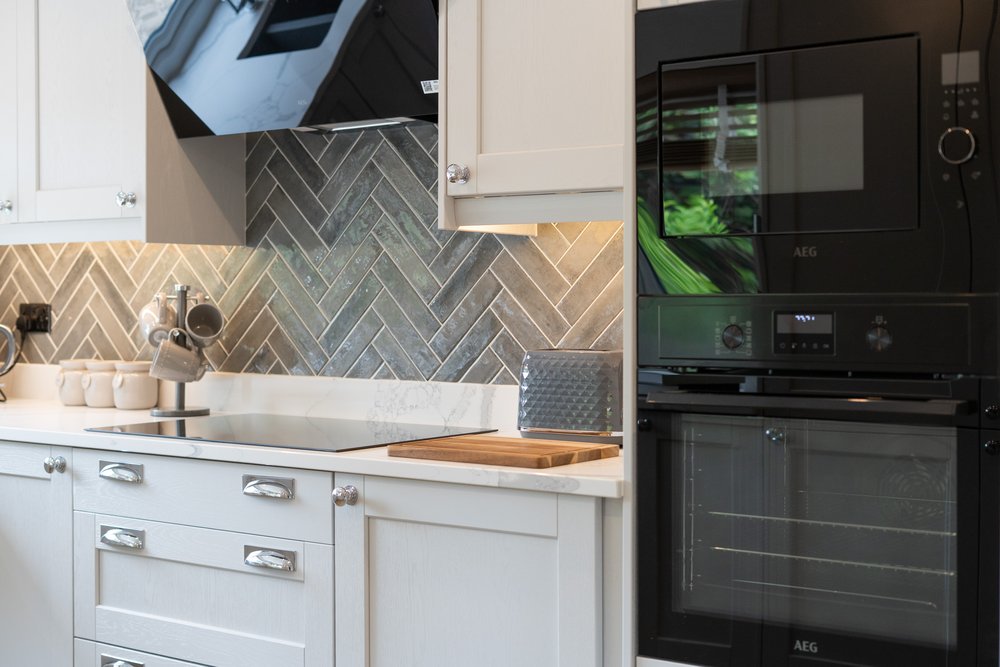 Close-up detail photograph of a kitchen hob, oven and herringbone tiled splashback